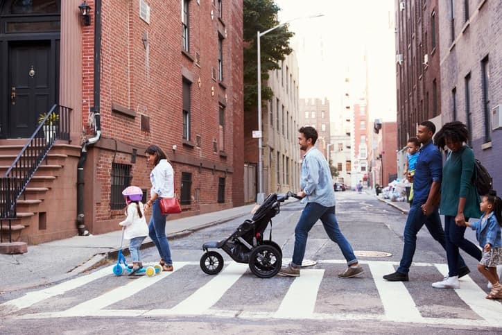 child on scooter, woman pusing baby stroller up to a curbcut